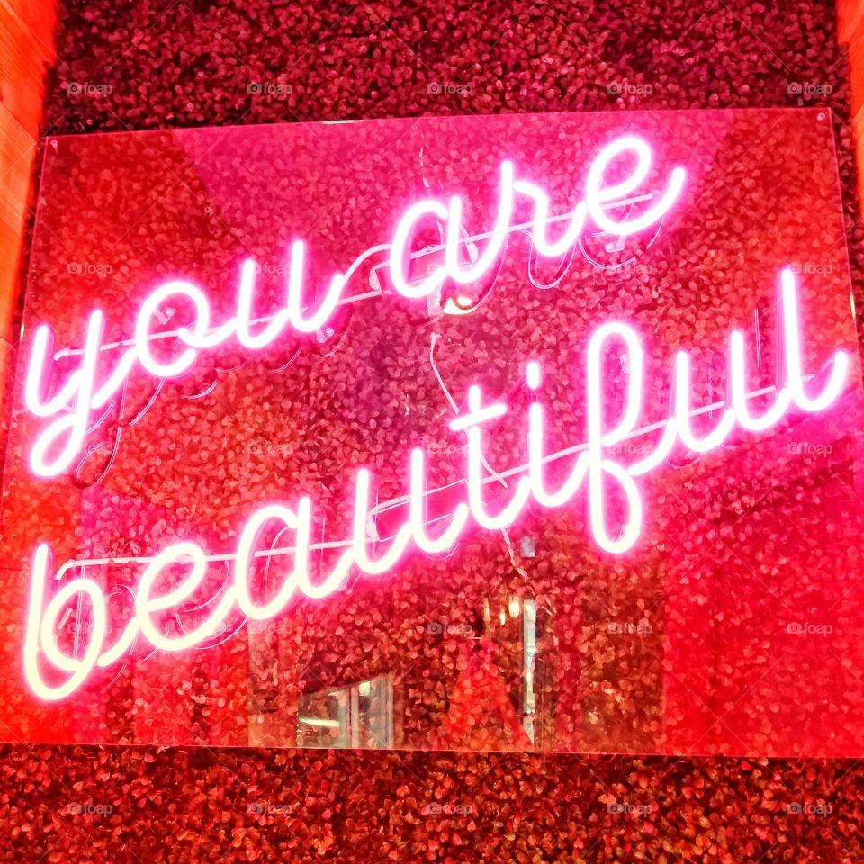 A neon pink sign with the words " you are beautiful " on it, hangs in a restaurant.