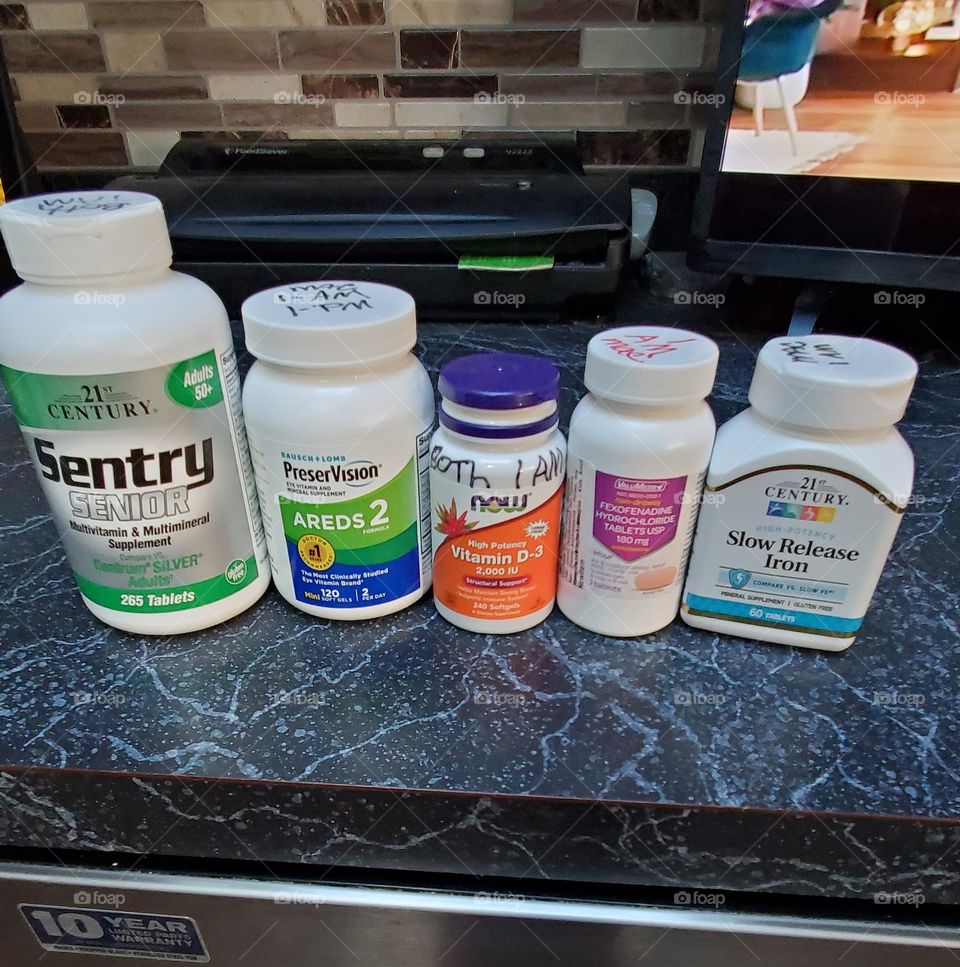 Supplement  bottles lined up on counter. Vitamins lined in a row by size. These vitamins promote good health and keep allergies under control. Different size bottles lined up.
