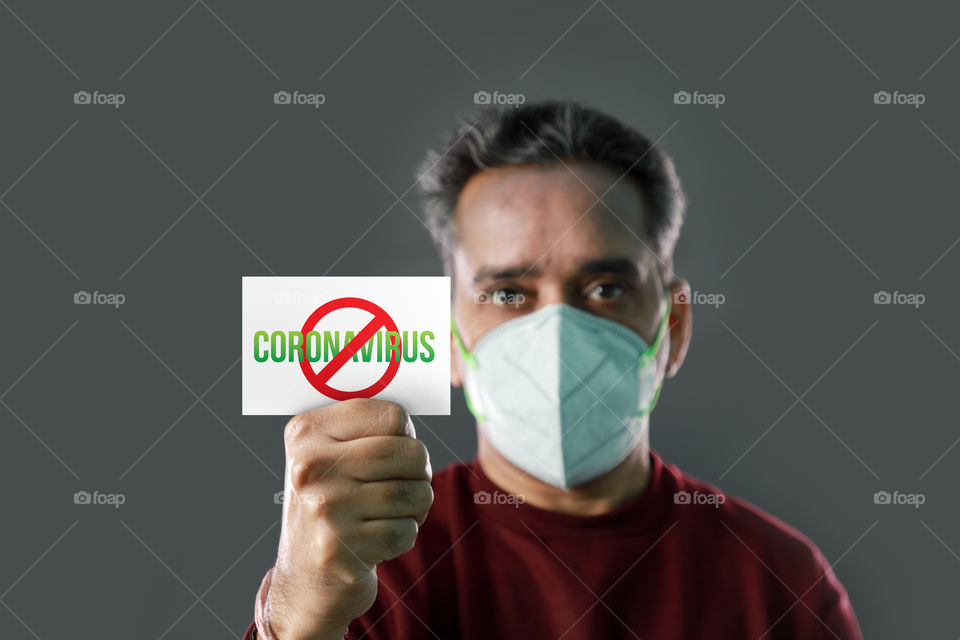 Indian man with stop corinavirus spread card in his hand, wearing a mask