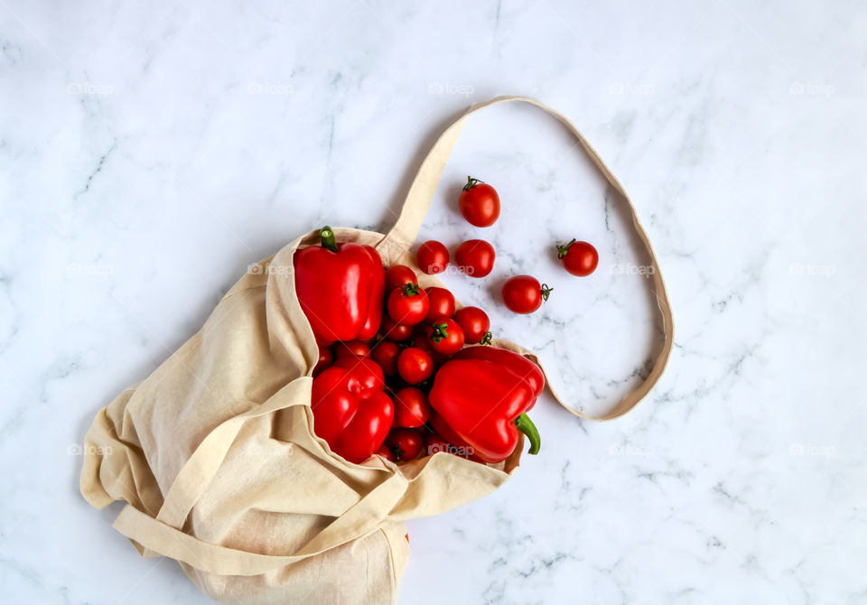 Red vegetables in a reusable linen bag on marble background. Eco-friendly concept.