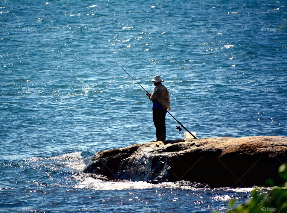 A solitary man with his fishing rod a bucket and bait. Ocean fishing and time to think.