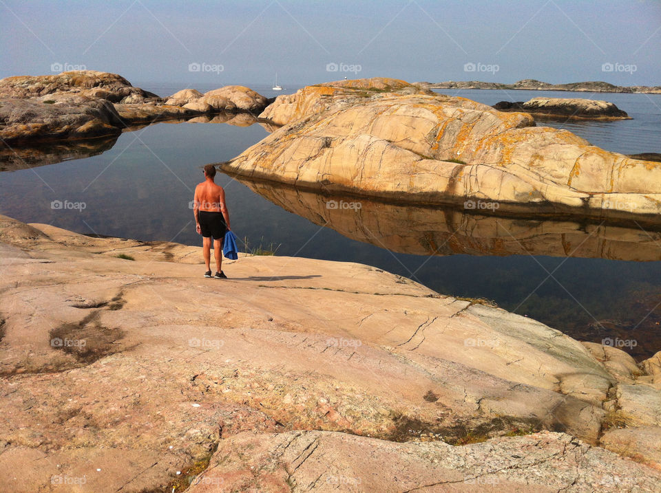 Peaceful . One man standing on the rocks a sunny morning, looking at a peaceful sea.