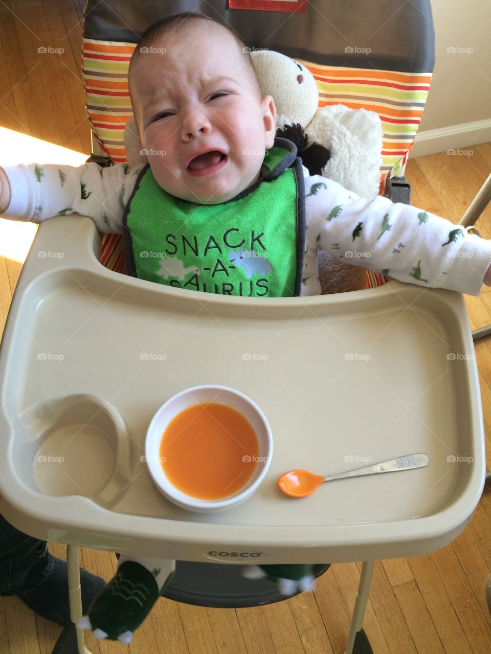 Crying baby sitting on dinning seat with food in bowl