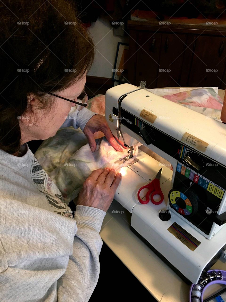Woman working at sewing machine fixing clothes & making alterations to projects piled up.
