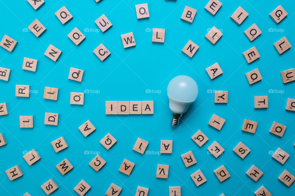 Word Idea formed by wooden letters in the composition center with all the letters of the alphabet on a light blue background with light bulb