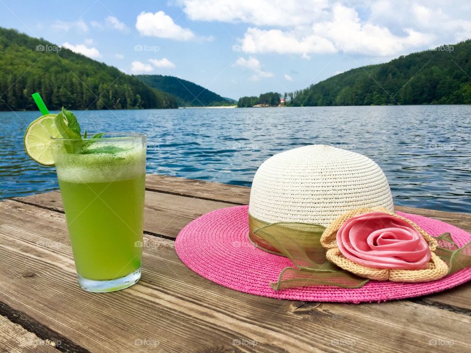 Mint lemonade glass and summer pink hat near the lake