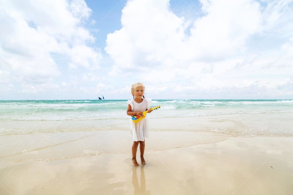 Little Caucasian girl playing on small guitar on beach 