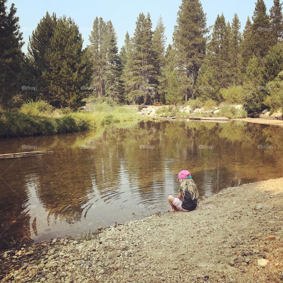 Girl sitting at lakeside with ripple in the water 