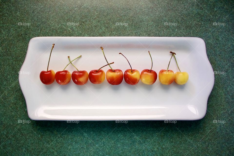 Fruits! - Rainier cherries arranged horizontally by color gradation on a white rectangular plate on a green surface in natural light