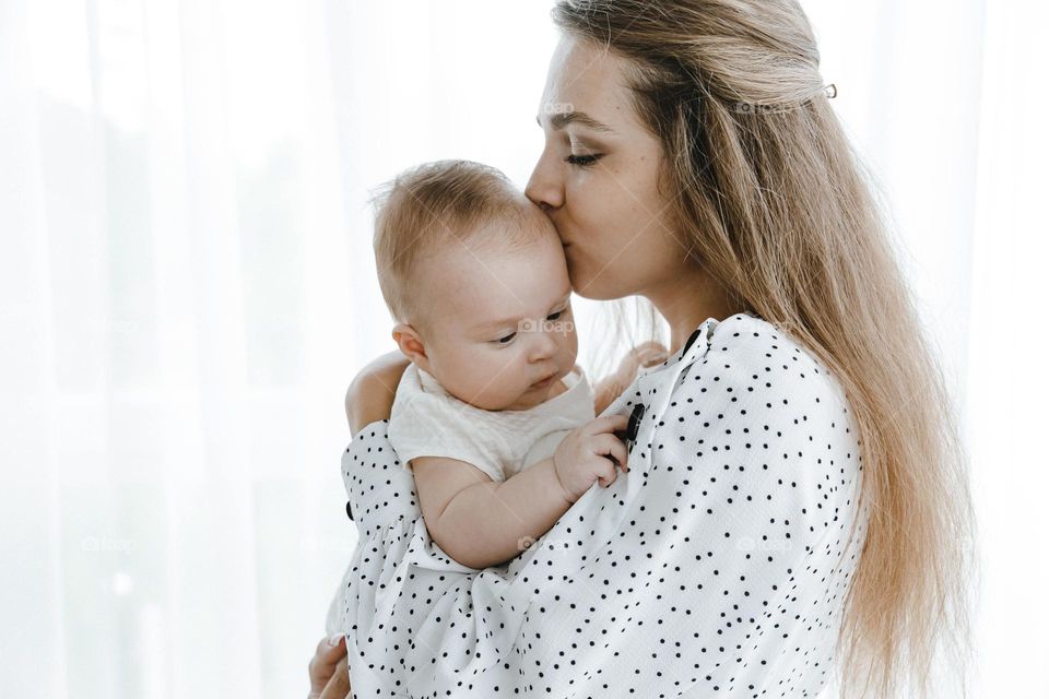 Mom in white dress with black polka dot holding baby and kiss on the forehead