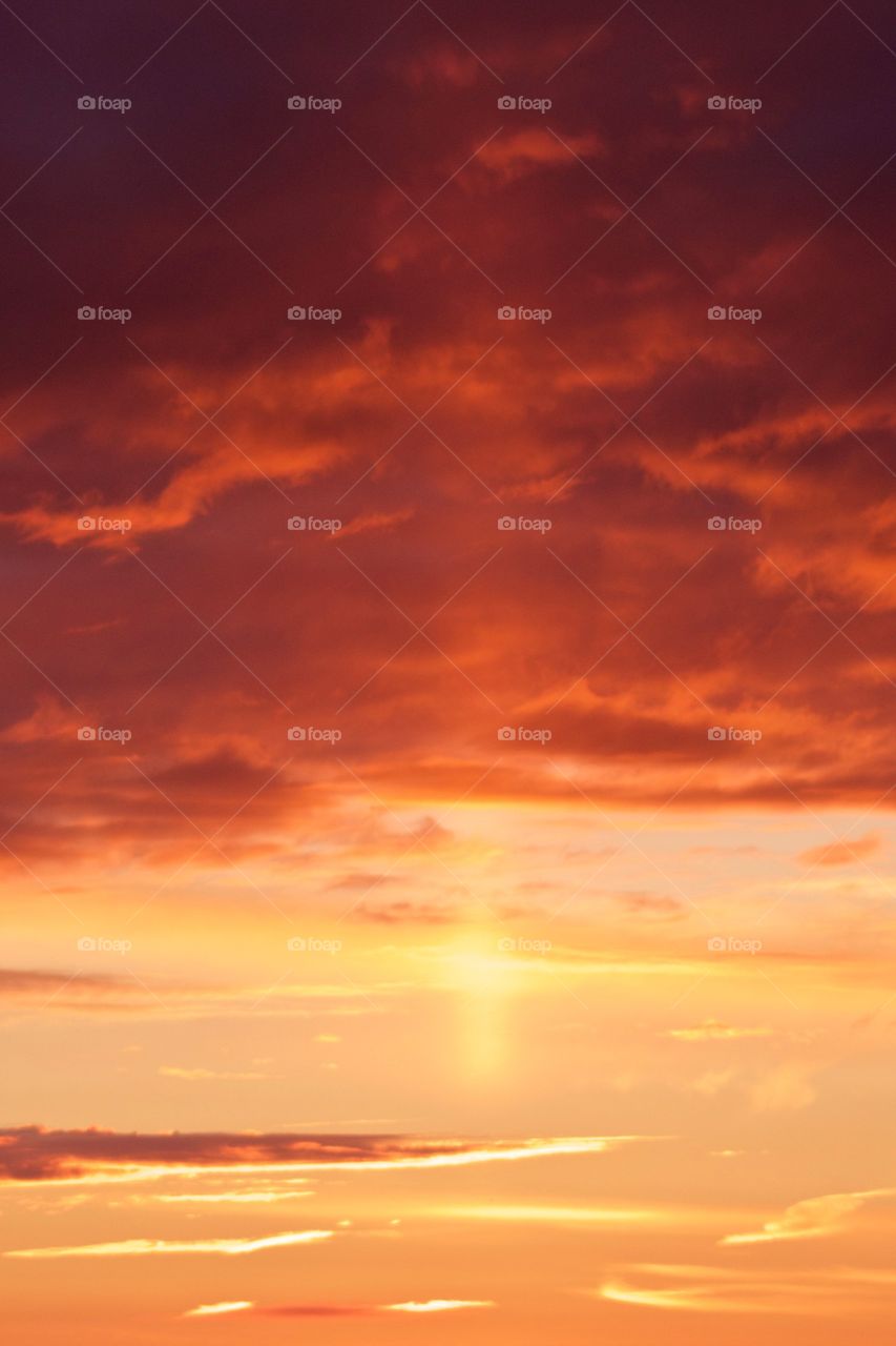 A canopy of brilliantly colored orange and yellow clouds in a pastel-yellow sky with a single vertical ray from the sun