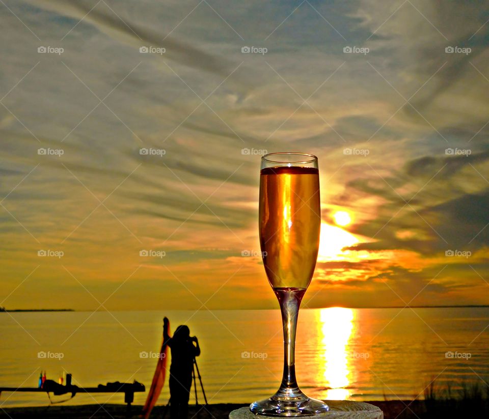 Liquids - A colorful glass of wine while watching a photographer takes sunset photos as the golden sun descends below the horizon