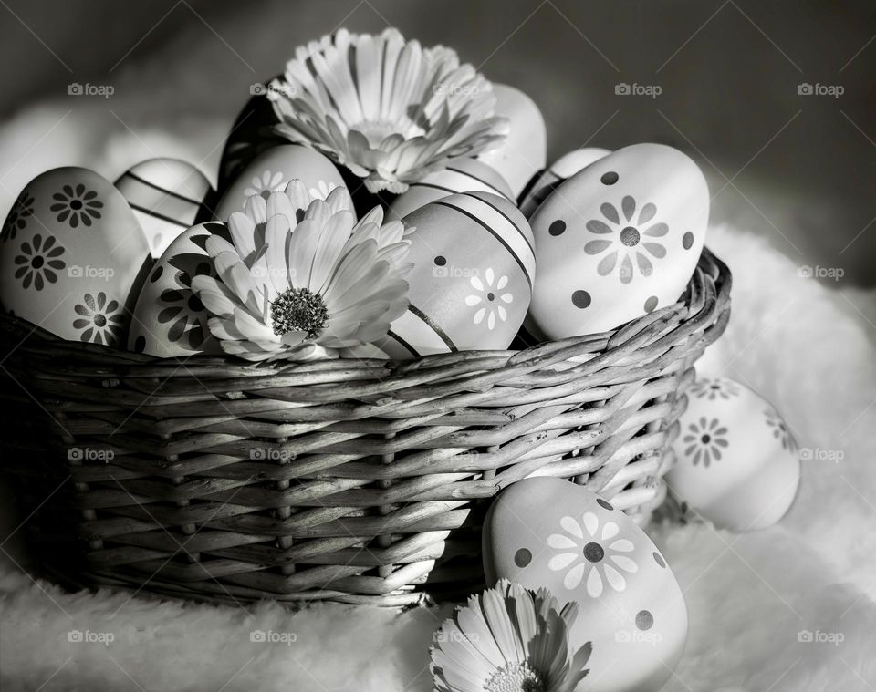 A basket of decorated eggs and flowers on a soft white blanket