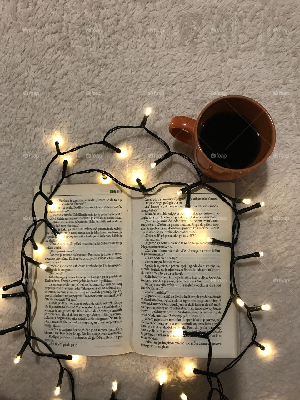 Look from up above onto the opened book, yellow Christmas lights, and a warm, orange cup of coffee.