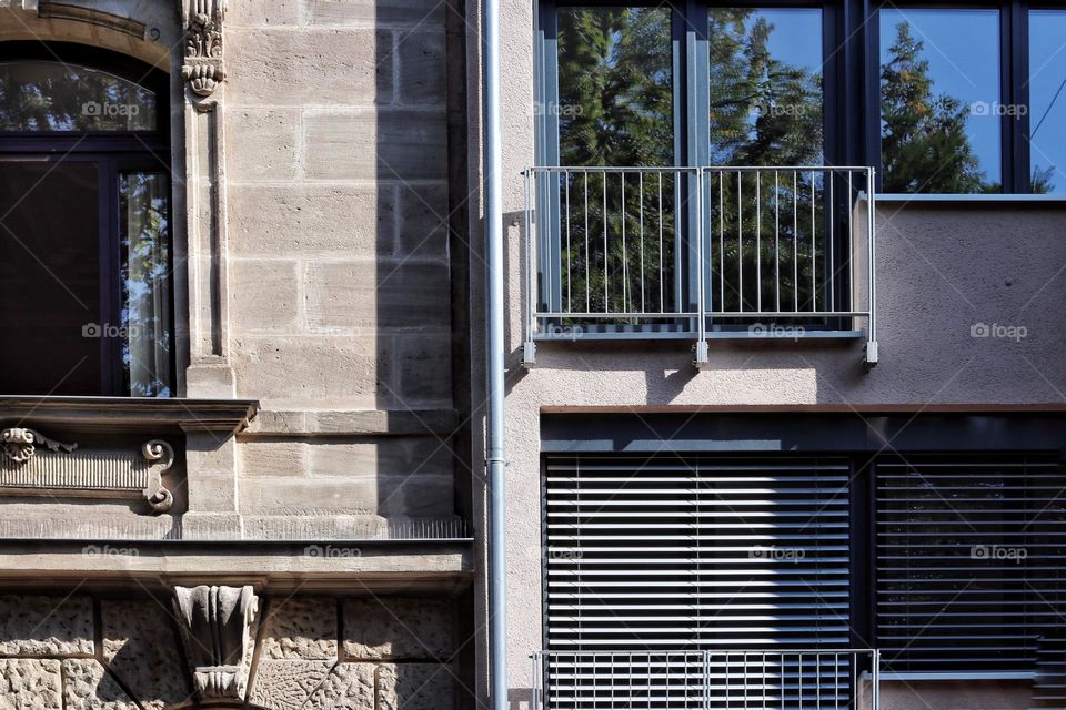 The contrast between a historic sandstone building with decorations and a simple modern building right next to it 