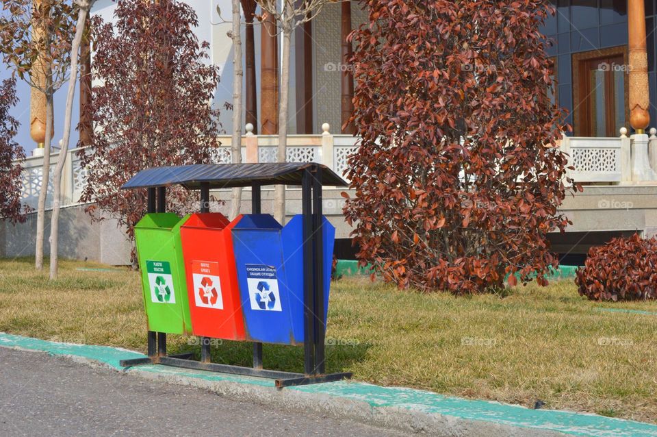multi-colored garbage container for collecting different types of garbage against the background of city buildings and plantings