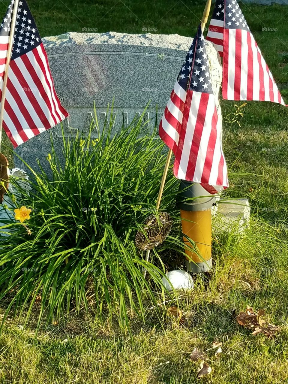Three American Flags displayed  on Soldiers grave, sunlit in late day. They look like newly placed flags.