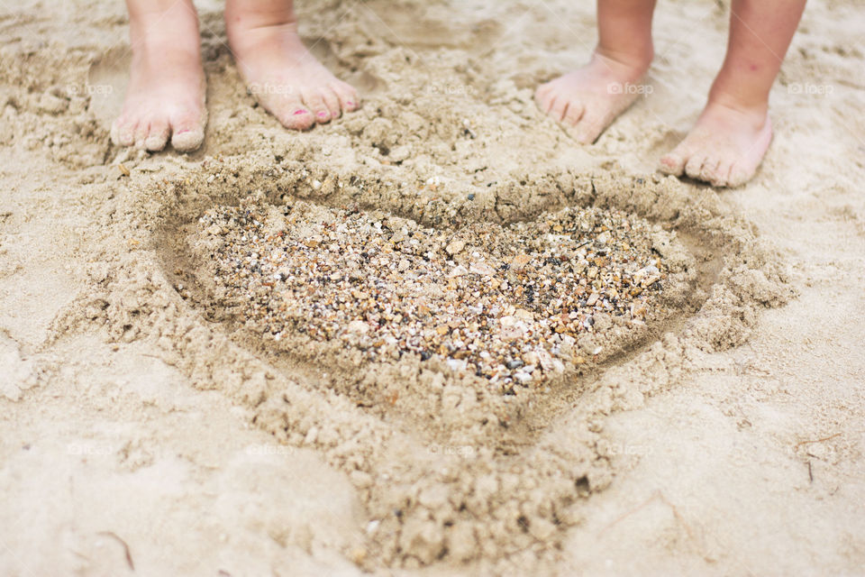 heart in sand with pebbles. heart made of sand and pebble with child feet on the beach