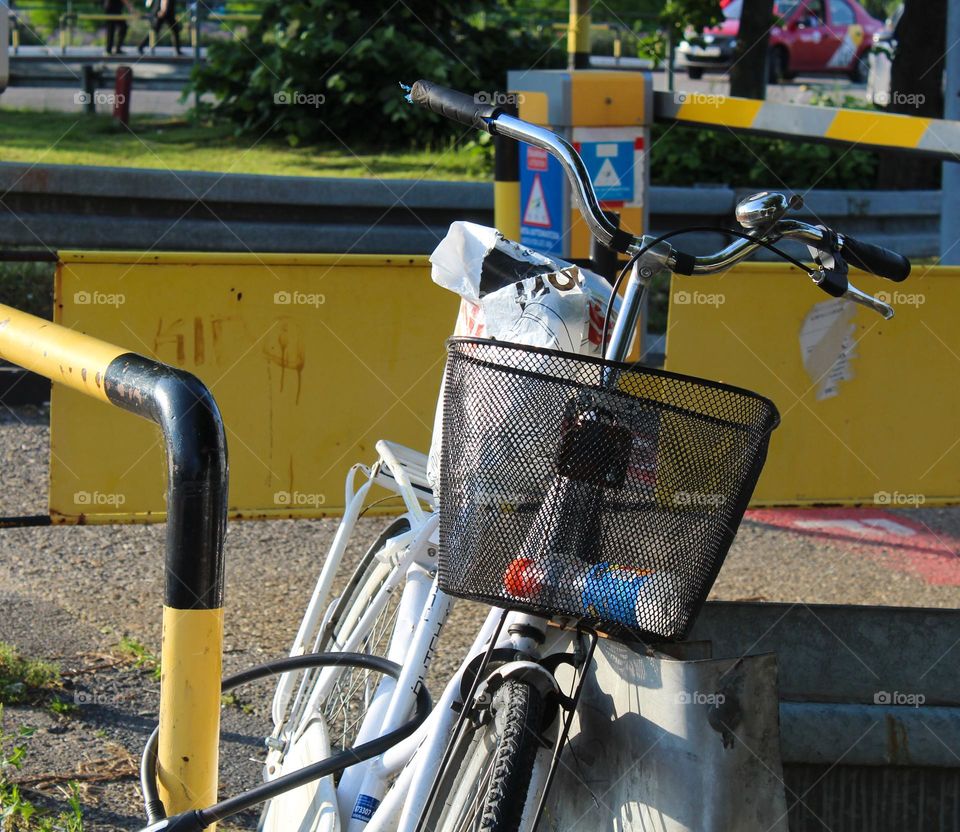 Close up of one white lonely bicycle with black basket locked to a metal fence.