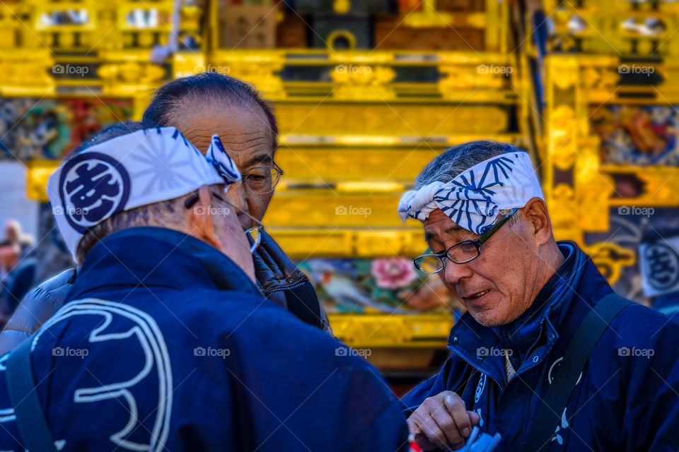 Detailed discussion among elders infront of a golden float before the start of a Japanese festival or matsuri procession.