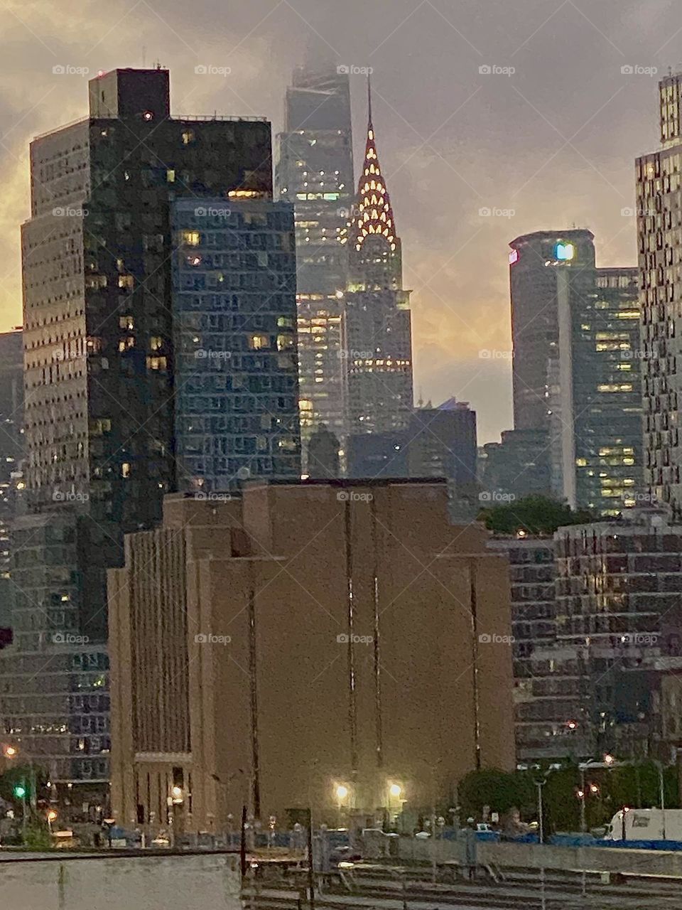 This is a closeup on the “Big Apple”, the city that never sleeps seen from atop the “Pulaski Bridge” at “Newtown Creek” in LIC, Queens at twilight time before nightfall. The “Kreisler Building” can easily be recognized. 2023. Hypnotic Productions