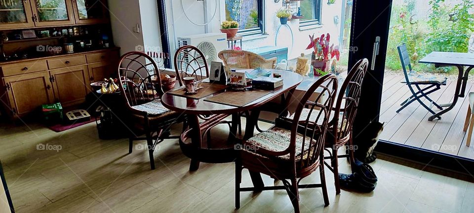 This is the third section of the L shaped living room in the house in „Bavaria“, Germany furnished with a more contemporary but old style table and chairs set. The large glass facade slides open giving access to the garden. 2023. Hypnotic Productions