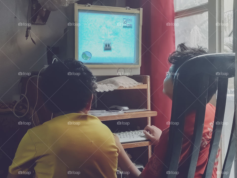 Two kids having a good time. One of them playing games on computer and the other watching him. Shot 1.