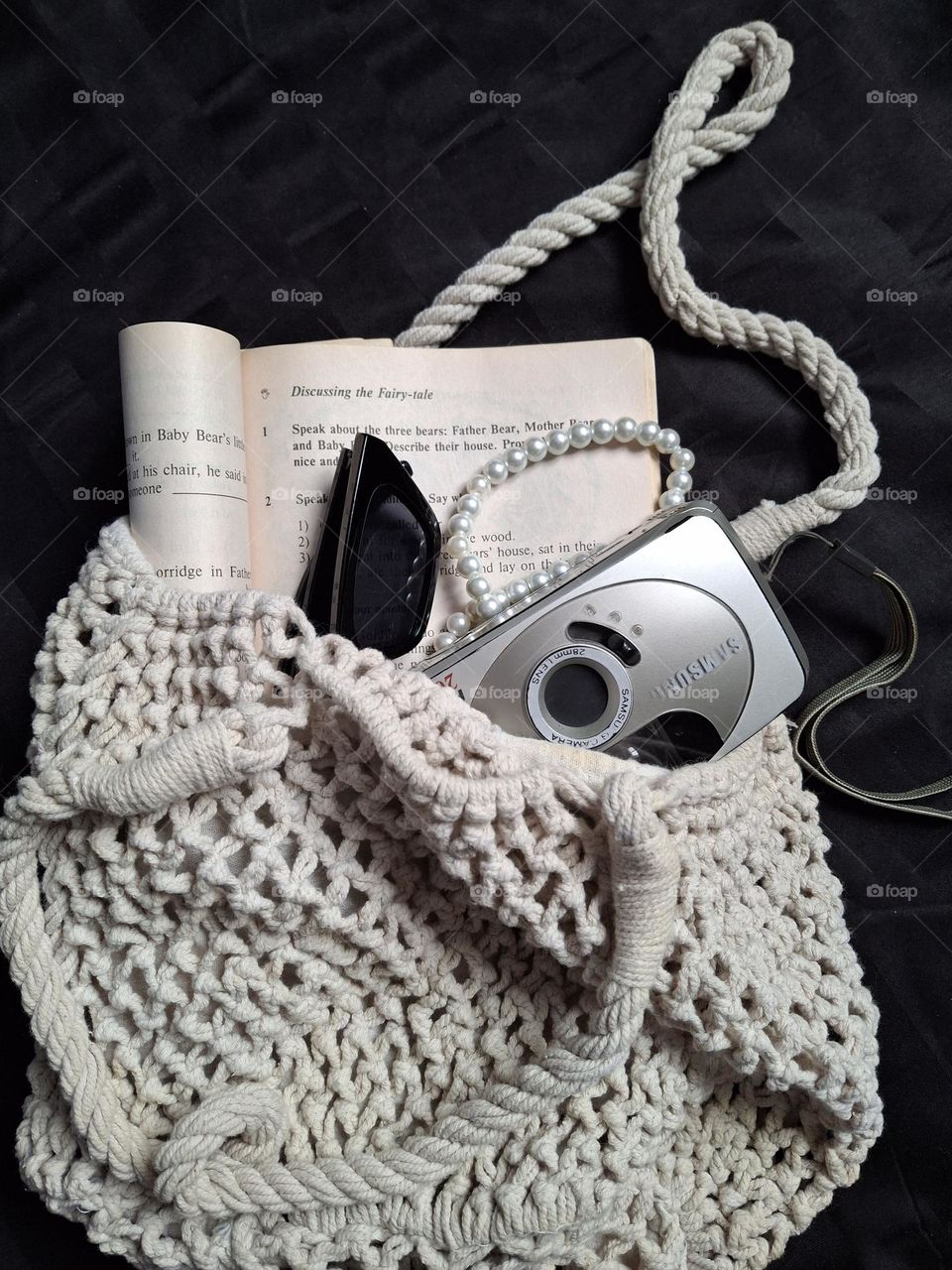 a woven retro bag filled with a retro camera, glasses and a book