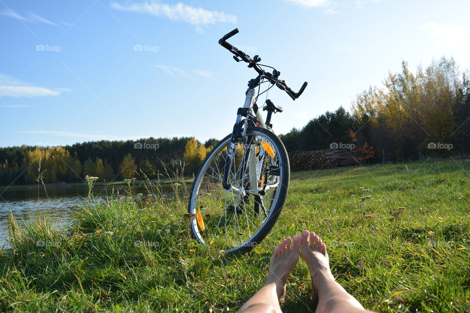 female legs barefoot resting on a lake shore and bike landscape