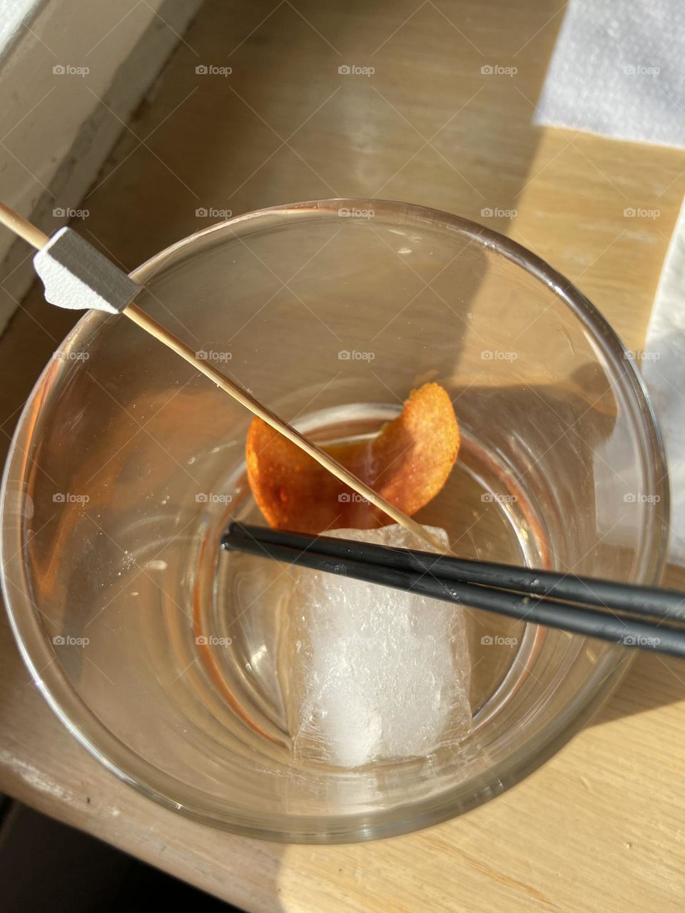 Remnants from a cocktail- ice cube, orange rind, stirrer, and straws in a cocktail glass. 