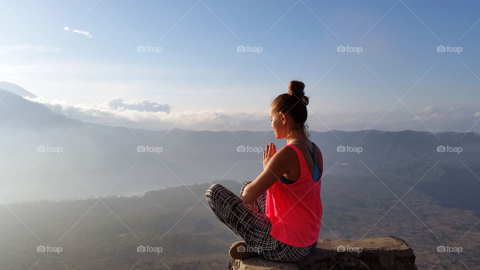 Young millennial woman meditating at the top of the mountain in Bali