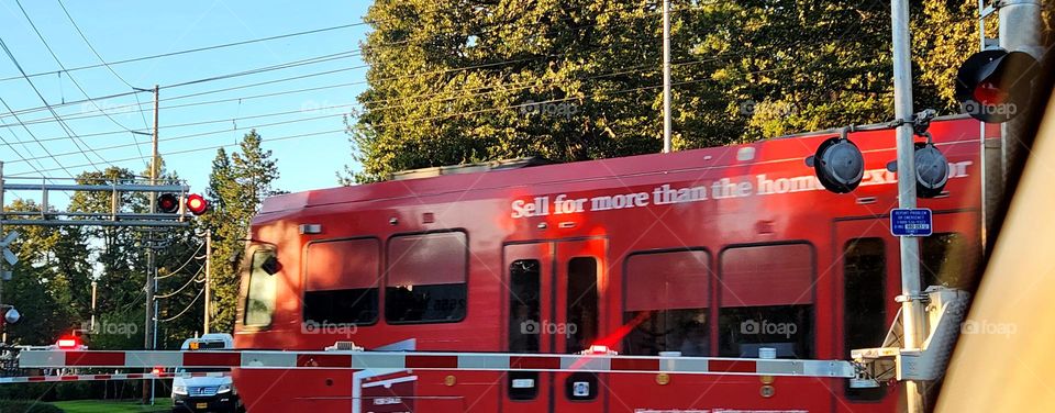 red public commuter train passing through Oregon on a week day evening while cars wait at the gate