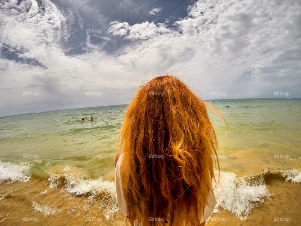 The girl looks at the ocean. Summertime.
