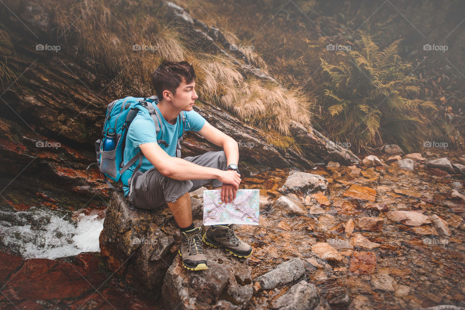 Teenager boy hiker sitting on rock with map