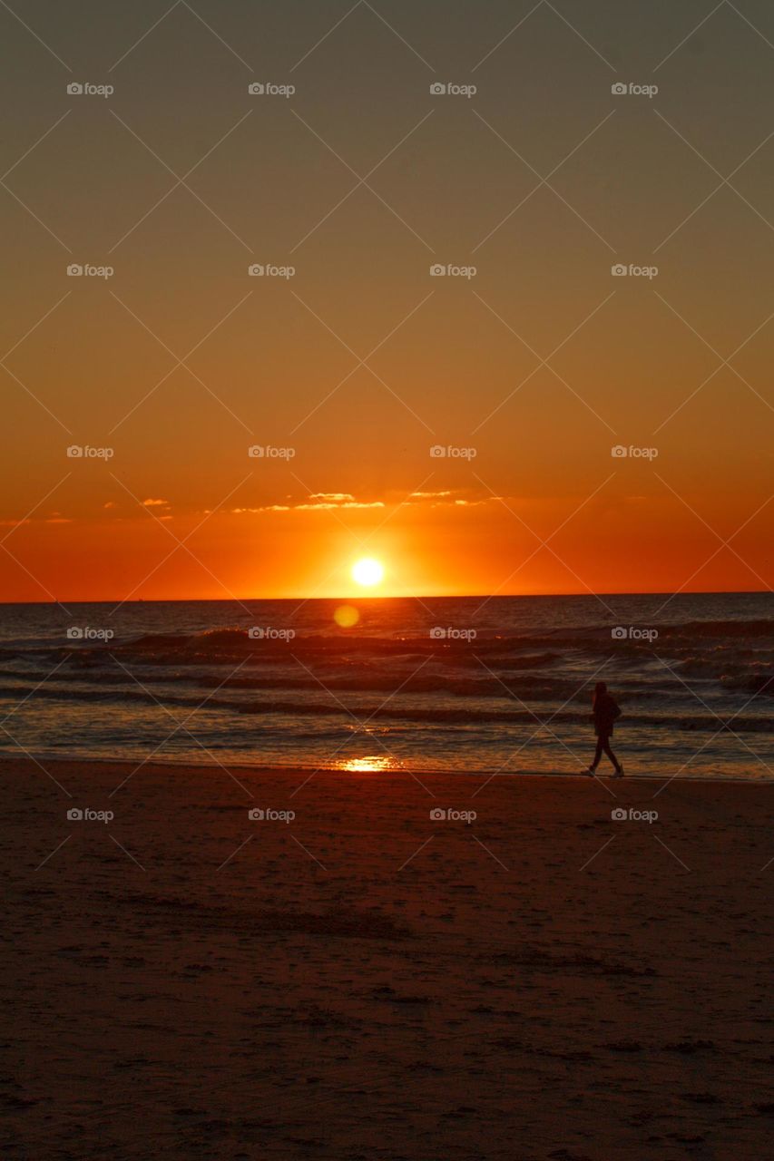 Person walking on the beach at sunset.