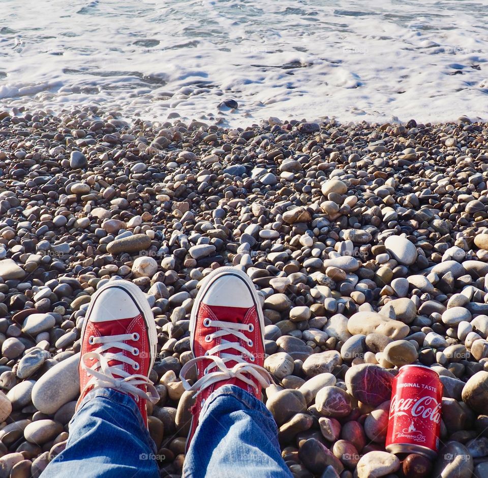 A can of Coca Cola on the beach with red sneakers.