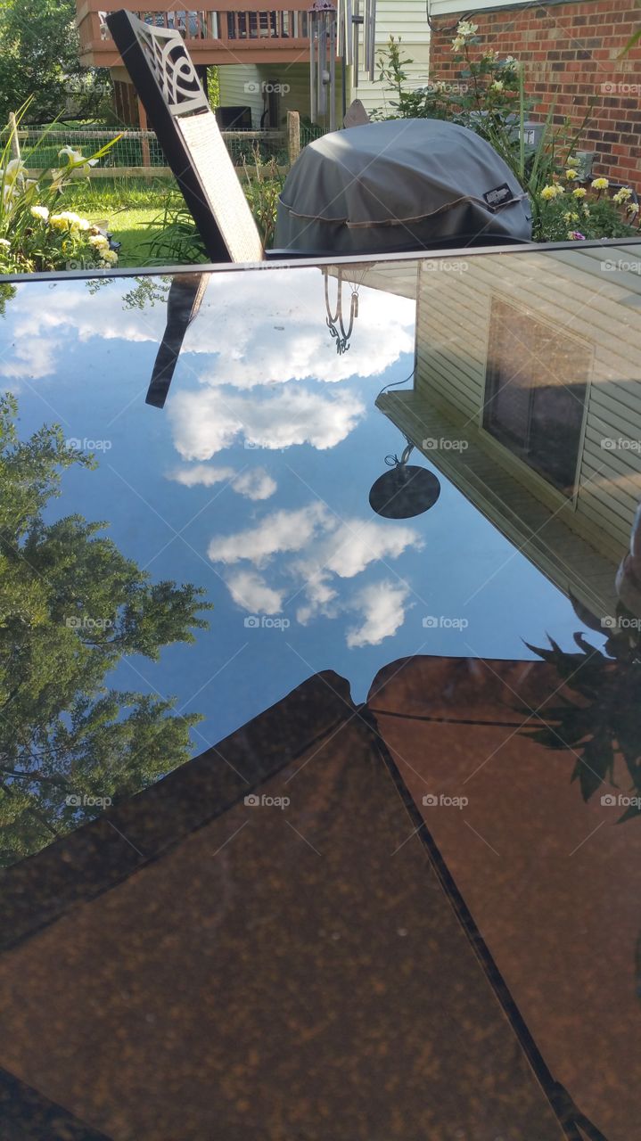 reflection on patio table. trees,  clouds and house reflected on my glass table,  looked neat. so I shot it.
