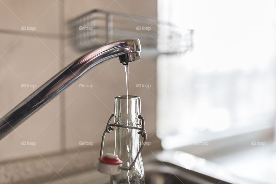 Glass bottle with clip closure under the water tap.