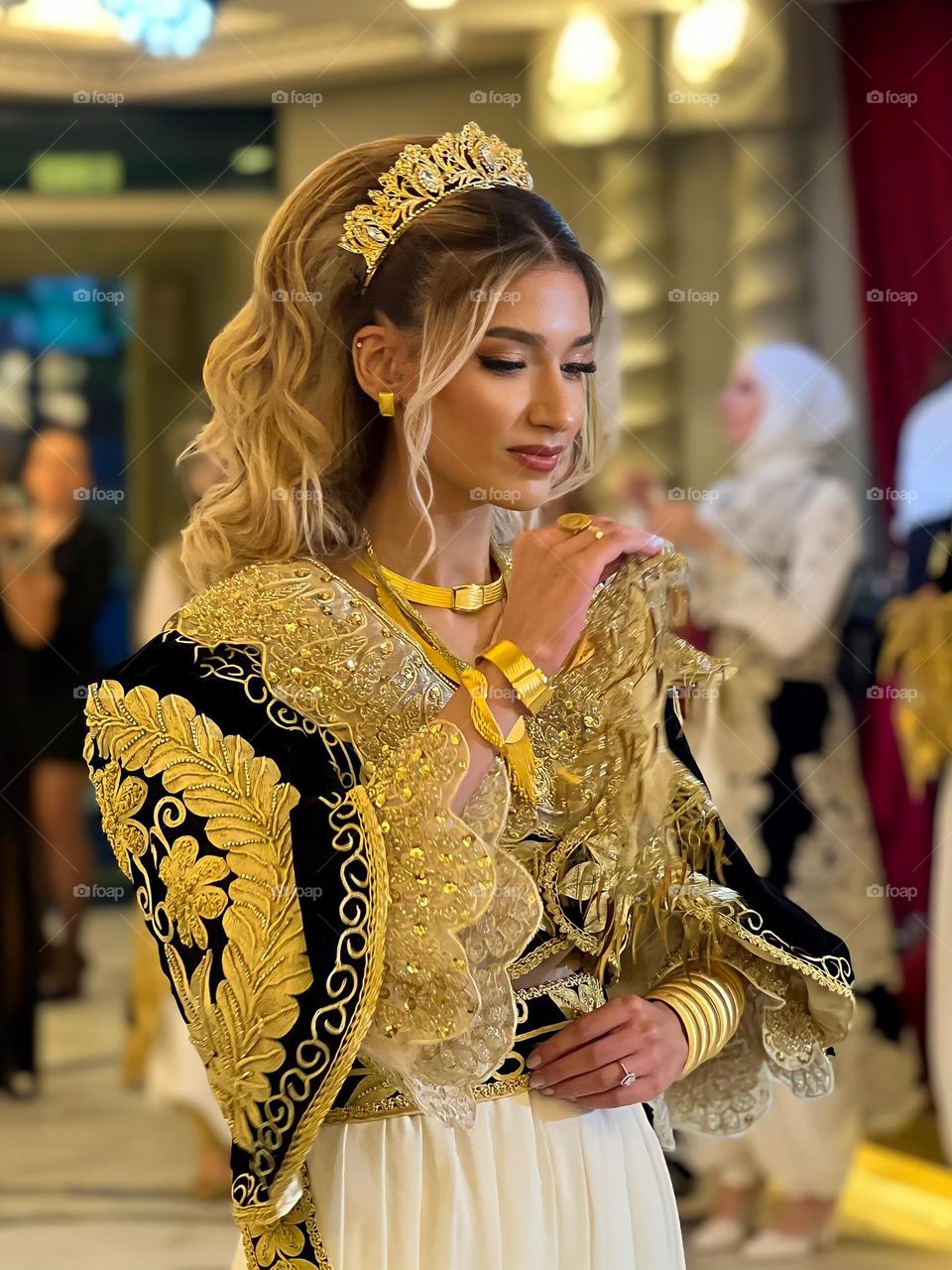 Close-up of a young woman wearing a luxurious gold-colored traditional dress with intricate embroidered details, and a crown