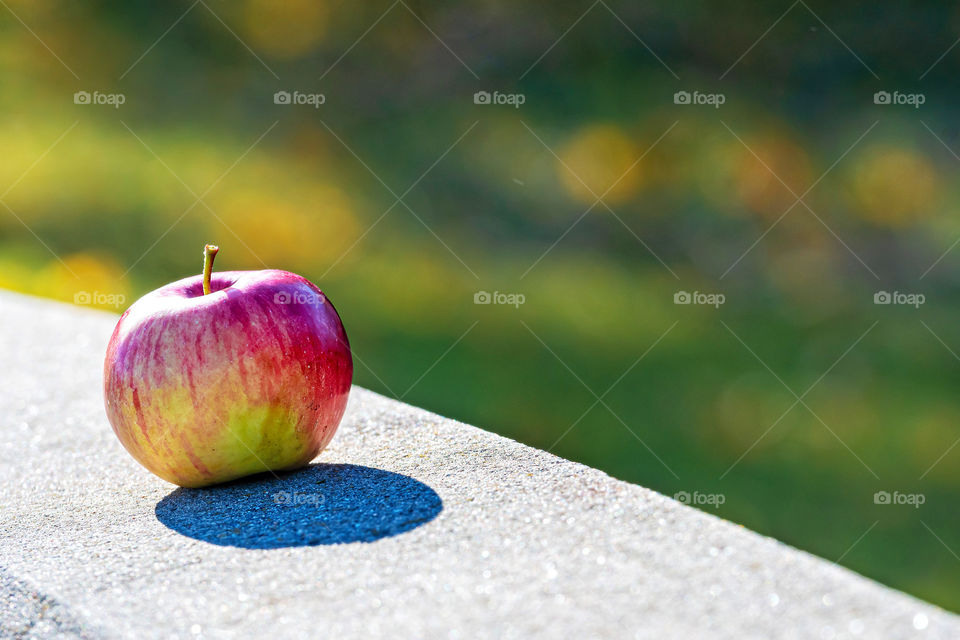 Lonely apple with shadow on a sunny day on the granite curbs. Selective focus. Blurred background.