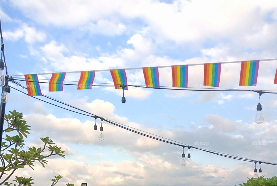 Six small pride color flags on a line against a blue sky at the end of the day