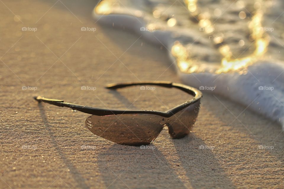 sunglasses under wet sand near waves