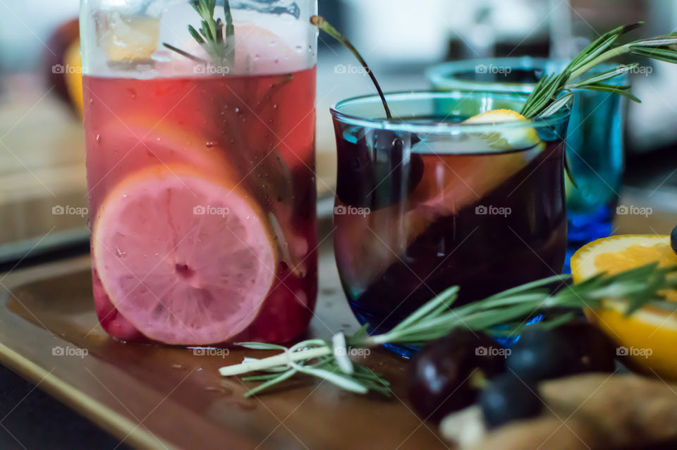 Low angle view of homemade juice and flavored aromatic water with cherry, blueberry, citrus, Rosemary, mint ingredients on wood serving tray garnished in vintage blue glasses for summer refreshments 