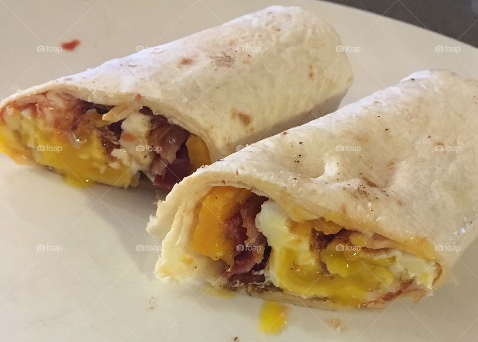 Breakfast burrito sandwich with egg, cheese and bacon cut in half on white plate