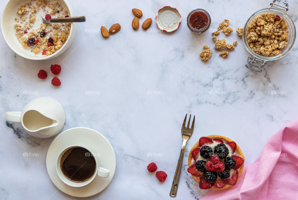 Top view to breakfast made by black coffee, milk, granola, fruits tarte, almond and jam with copy space.