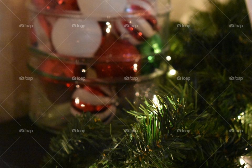 Closeup of a clear plastic bowl filled with ornaments, surrounded by a green wreath with white string lights. Photo takes place during the Christmas holiday season.
