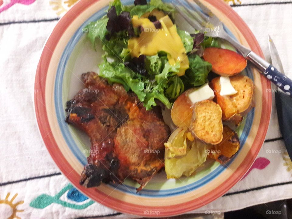 chuletas asadas, batatas y papa's asadas  y ensalada Verde. (grilled pork chops, baked sweet and regular potatoes and green lettuce salad)
