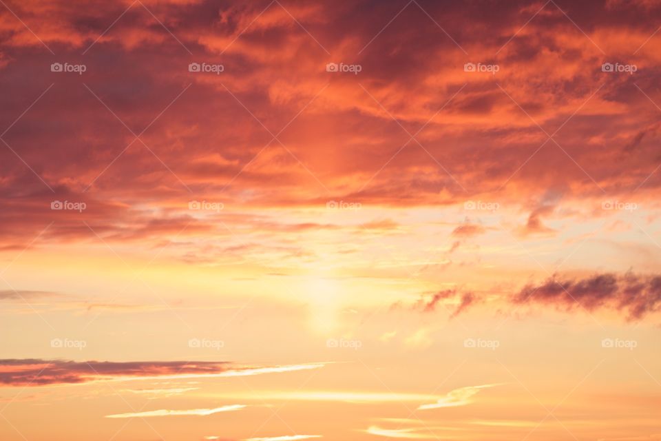 A canopy of brilliantly colored orange and yellow clouds in a pastel-yellow sky with a single vertical ray from the sun