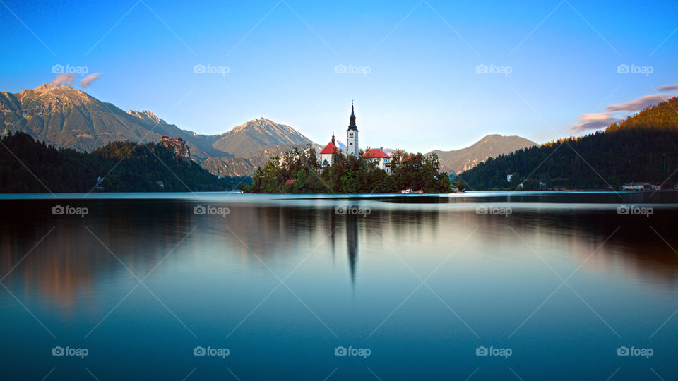 The enchanting Lake Bled with its island and the castle above the rock illuminated by the last rays of sun at the end of a late summer day.