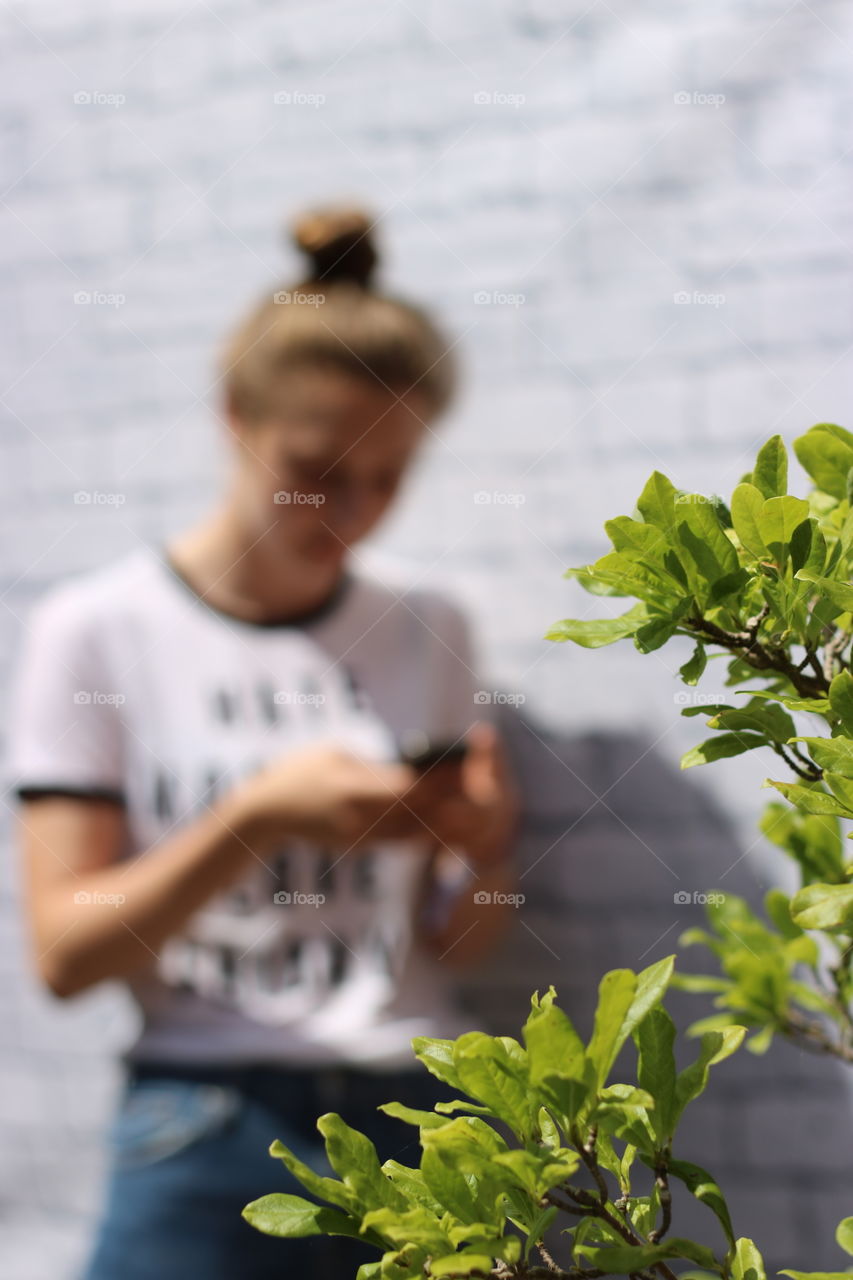 Close-up of green leaves near woman using mobile phone